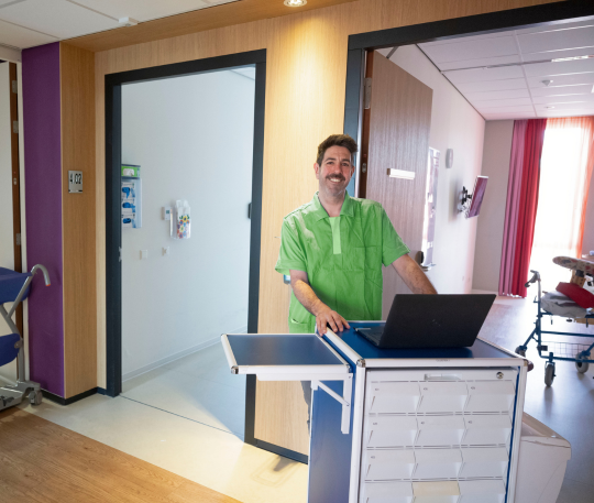 Verzorgende IG met laptop bij een werkstation in een zorginstelling.